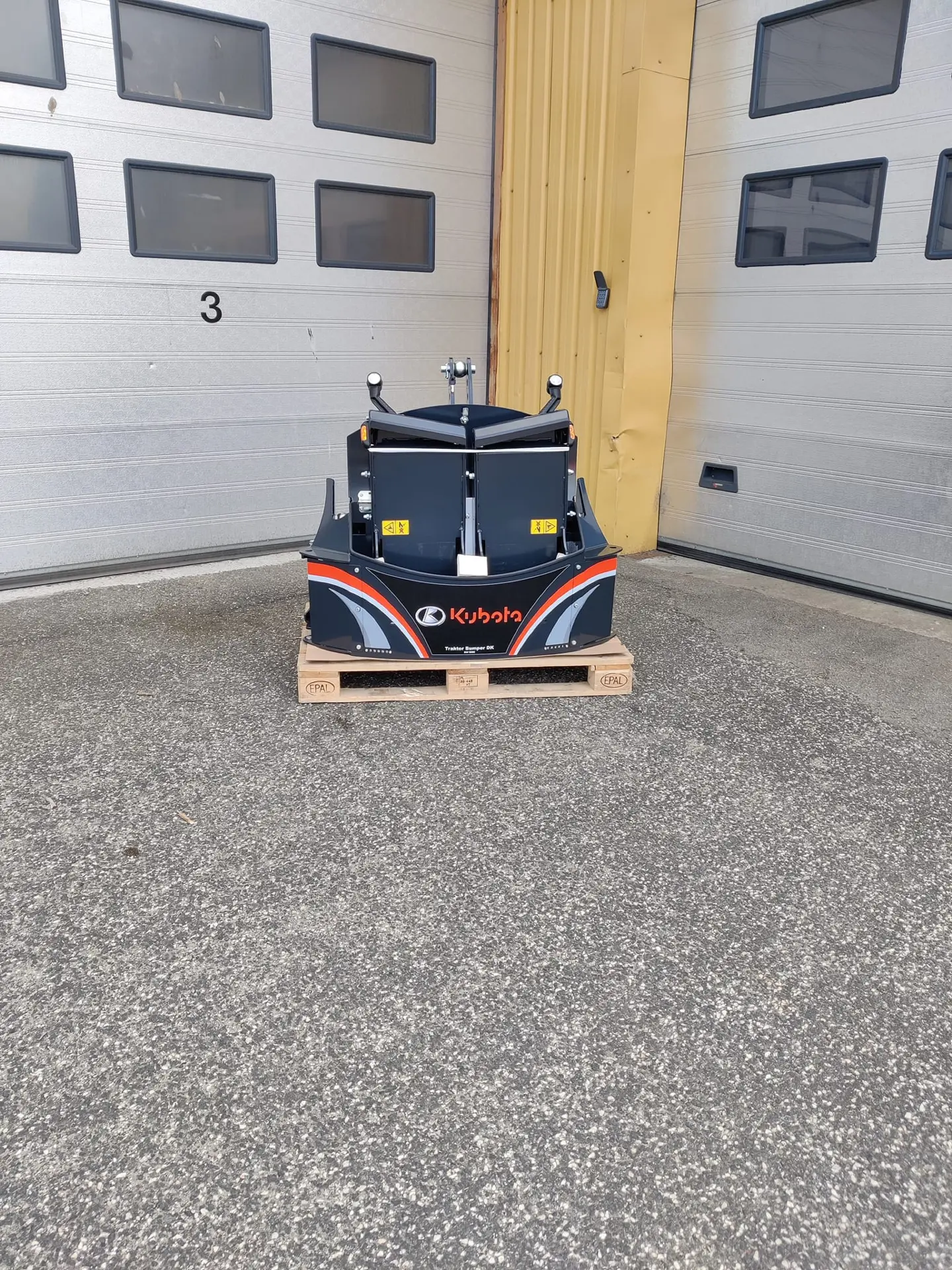 A Kubota front weight bumper for a tractor is displayed on a pallet in front of a garage door.