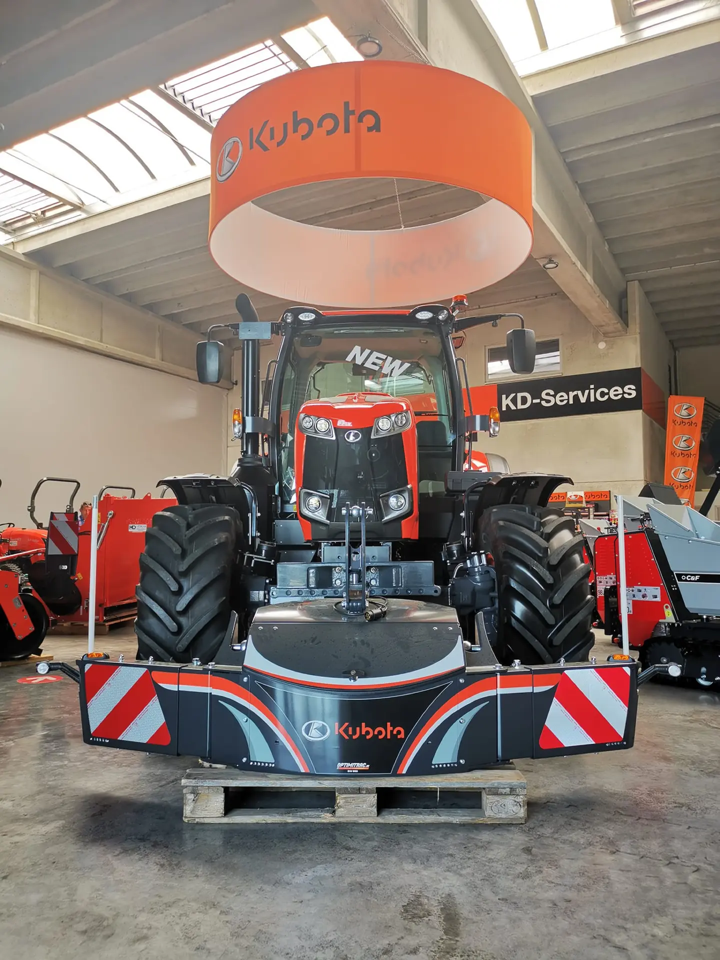 A front weight bumper with Kubota branding is mounted on a tractor displayed indoors on a wooden pallet