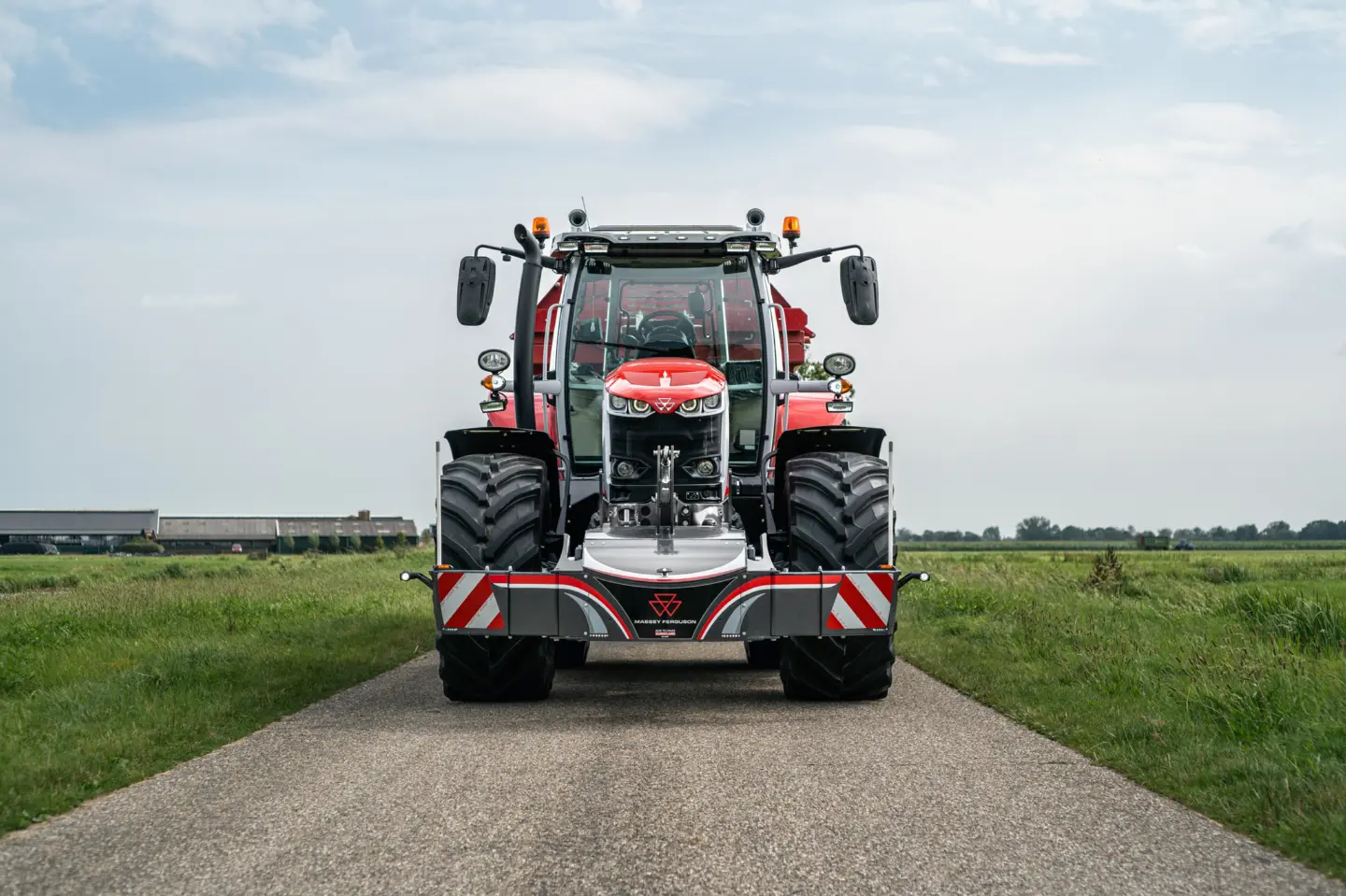 Red tractor with a front weight bumper, reflective safety markings and Massey Ferguson logo, parked on a rural road