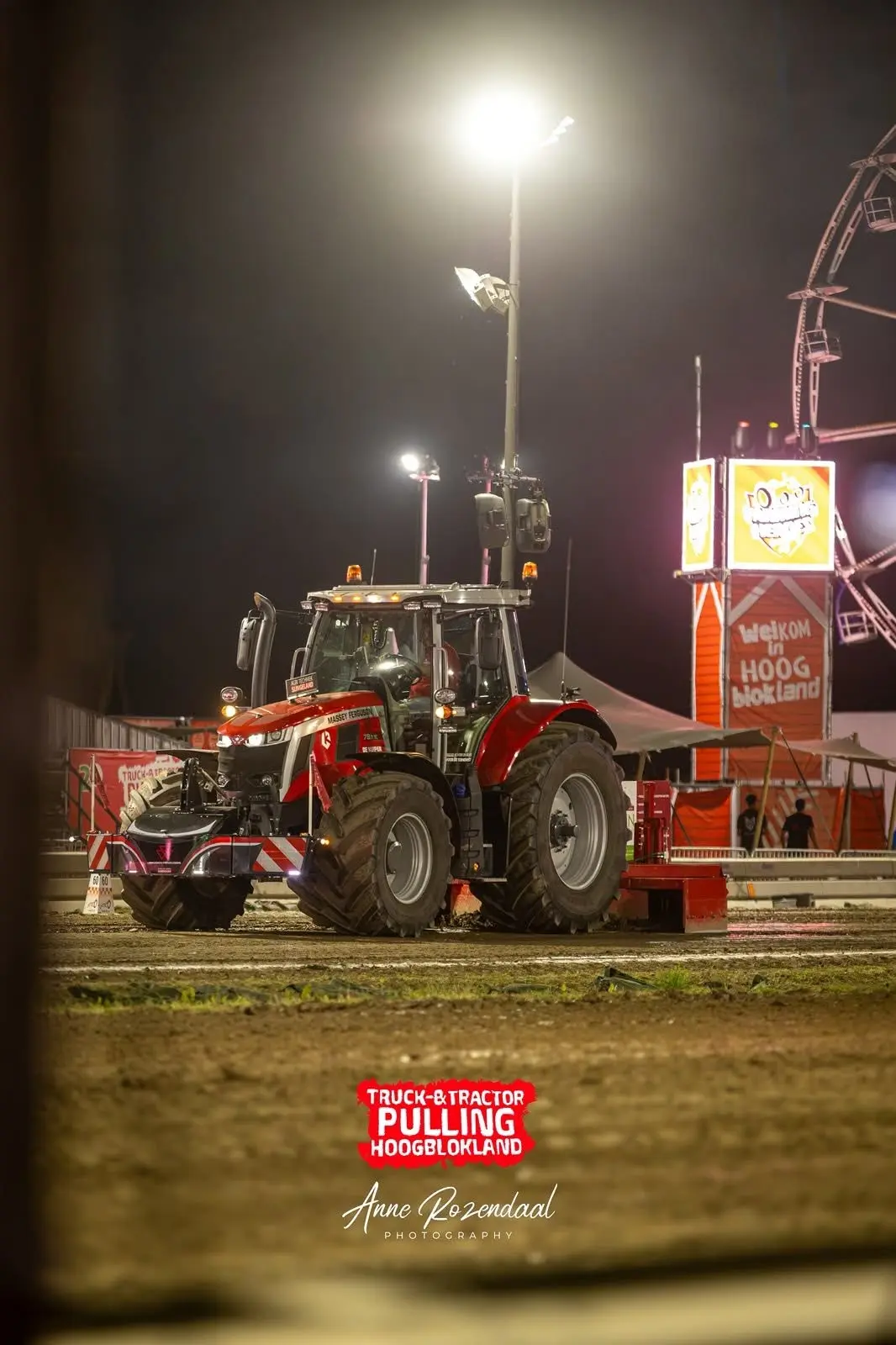 A red tractor with a front weight bumper is parked on a dirt track at night under bright lights