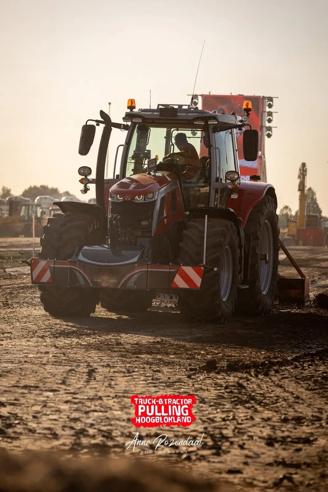 A red tractor with a front weight bumper drives on a dirt track at a tractor pulling event