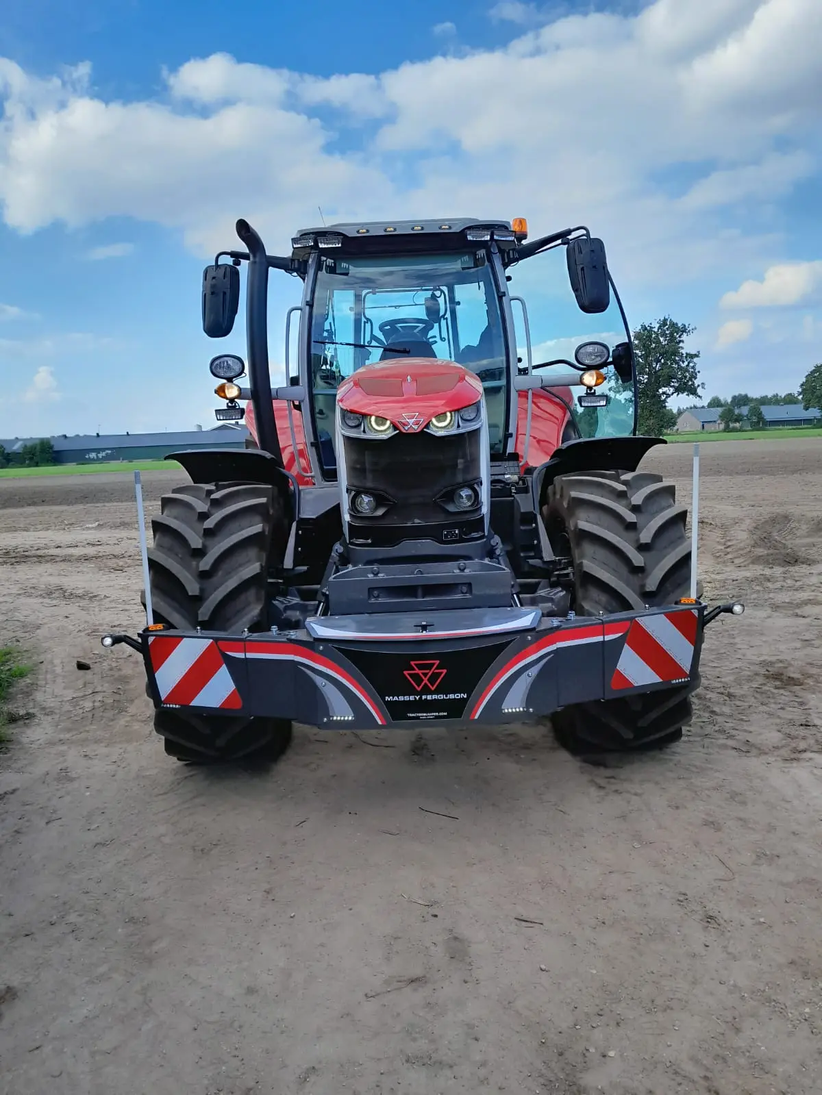 Red tractor with a Massey Ferguson branded front weight bumper on a dirt path, viewed from the front