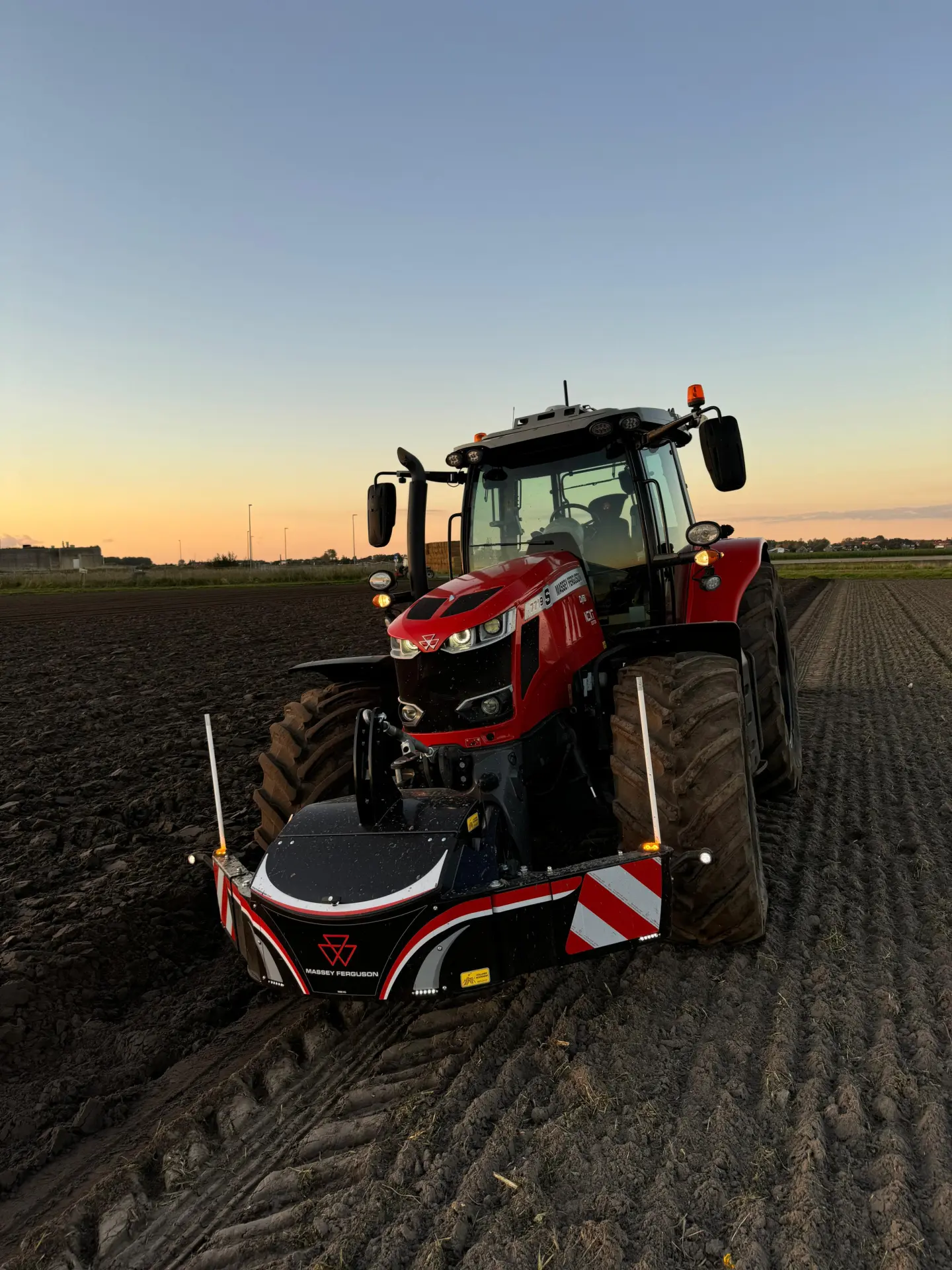 Red tractor with a front weight bumper attached, parked on a plowed field at sunset