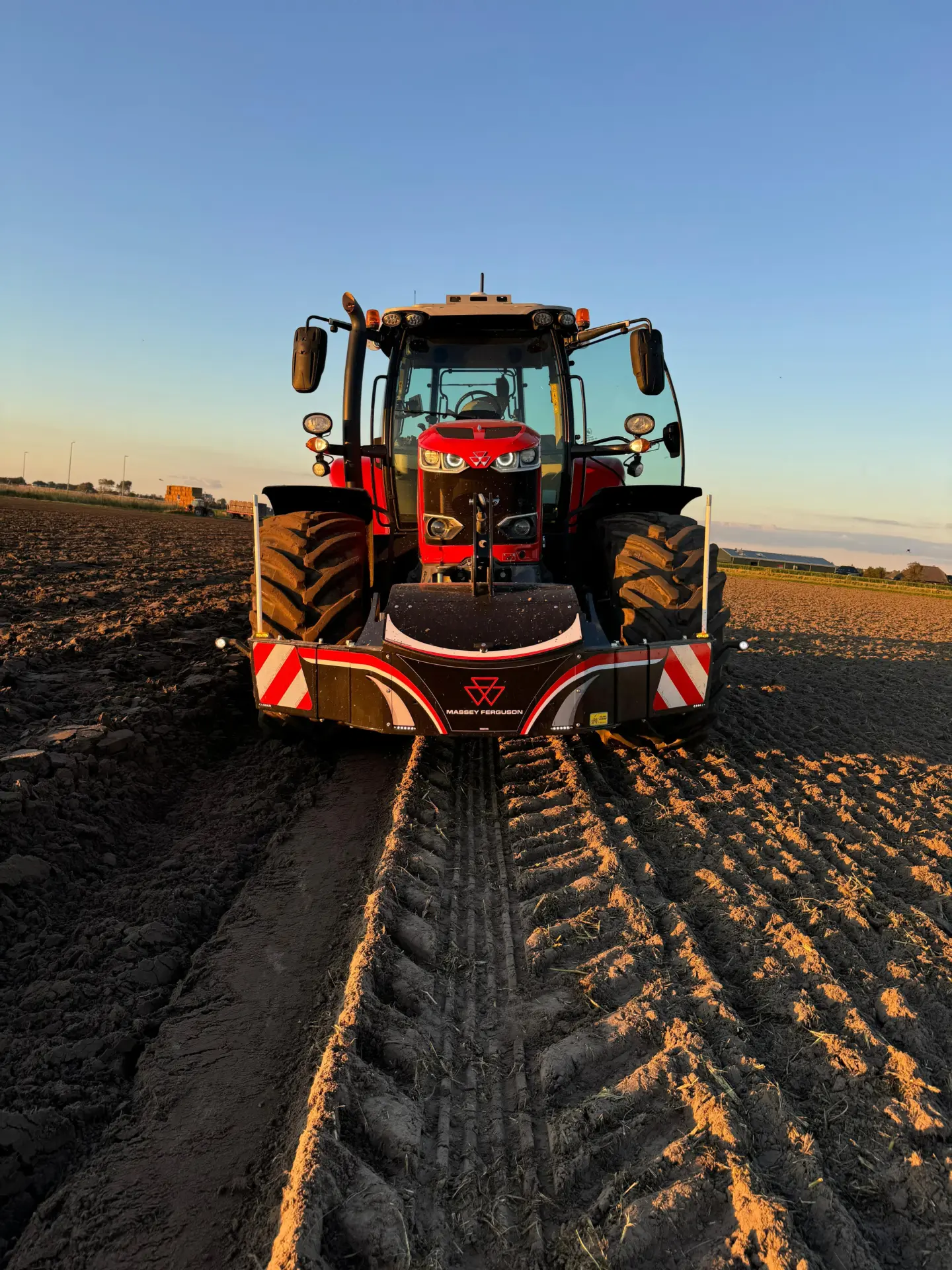 Red tractor with a Massey Ferguson front weight bumper parked on a plowed field at sunset