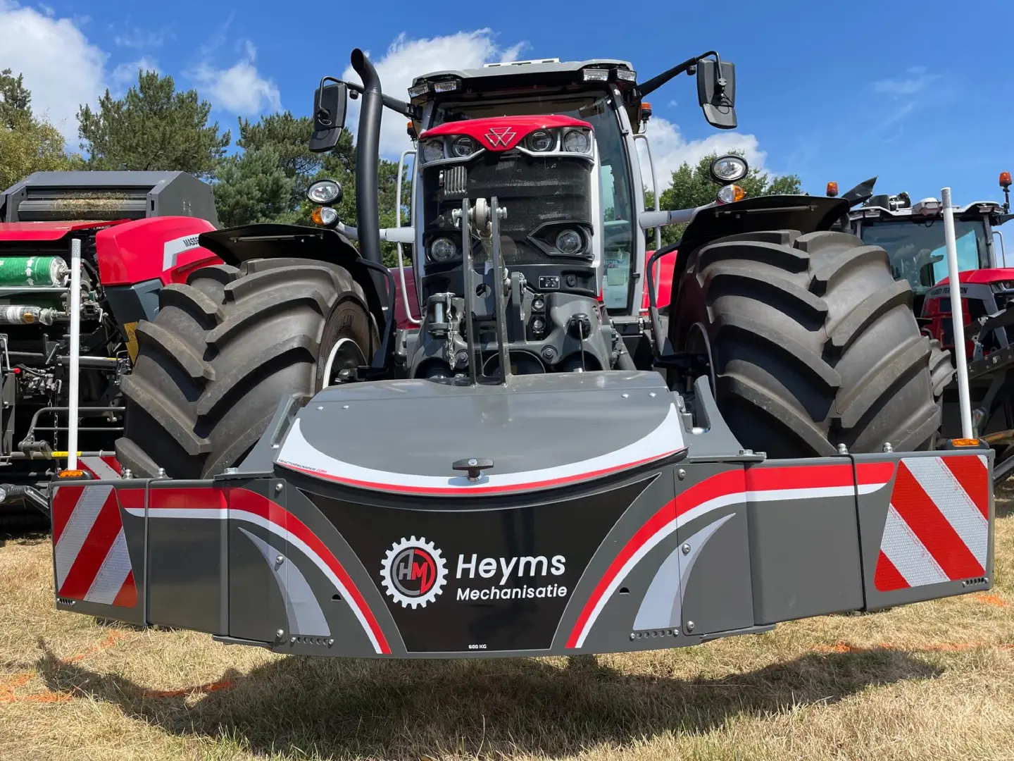 Large grey front weight bumper with red and white stripes mounted on a red tractor, with tractors in the background