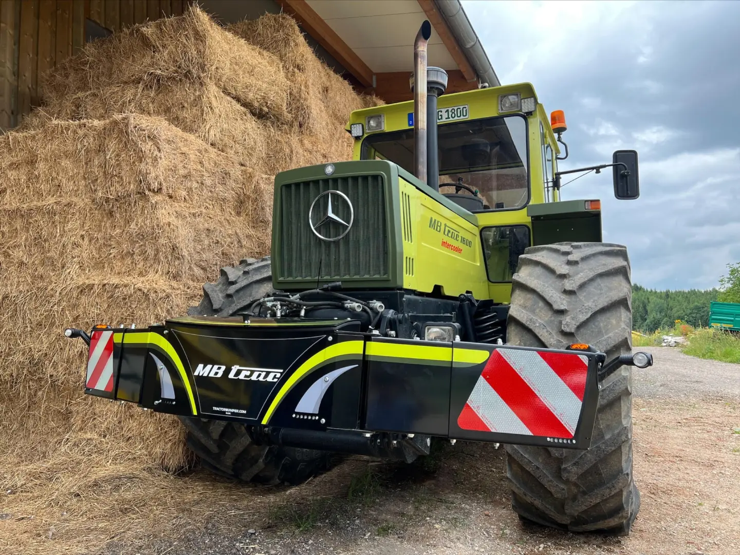 A green tractor with large tires is fitted with a front weight bumper featuring reflective red and white stripes