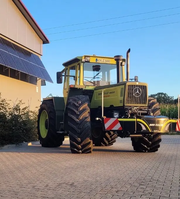 Large green tractor with a front weight bumper featuring red and white reflective stripes, parked on paving stones