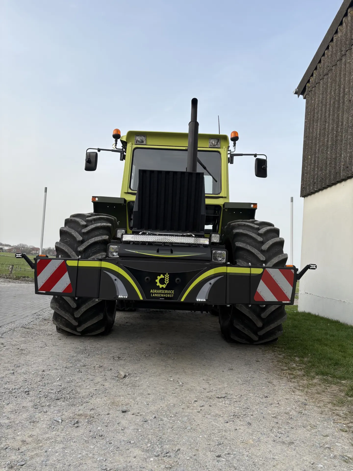 Large green tractor with a black front weight bumper featuring reflective red and white stripes and LED lights