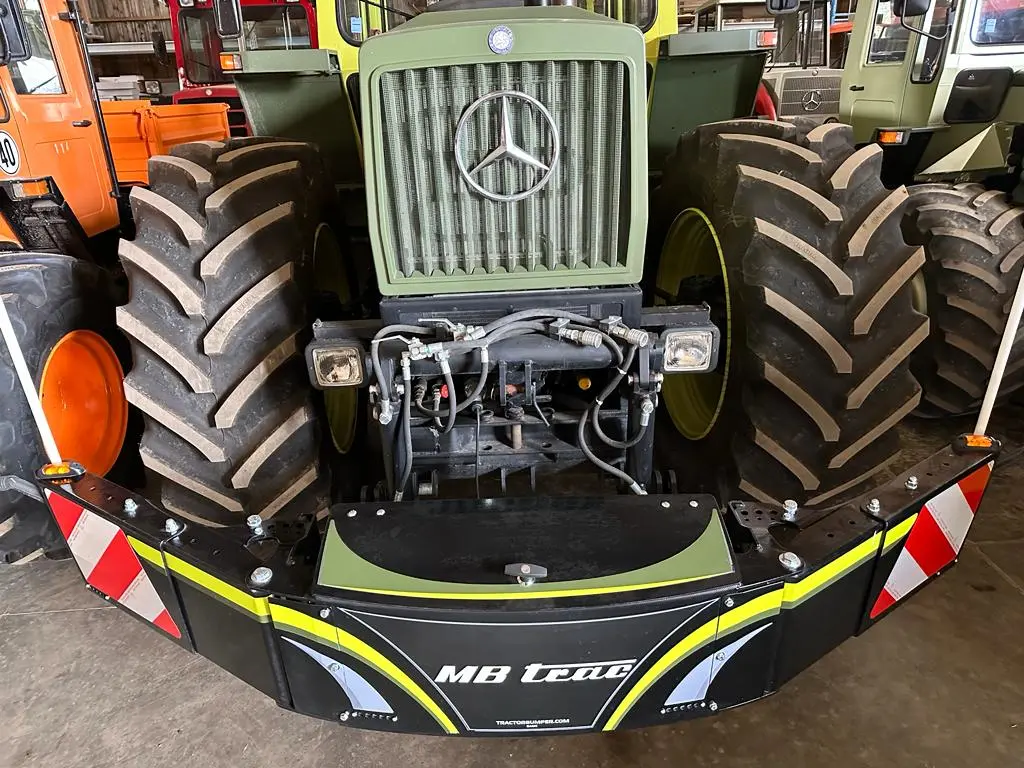Front view of a tractor with a mounted front weight bumper labeled MB trac, featuring reflective red and white stripes.