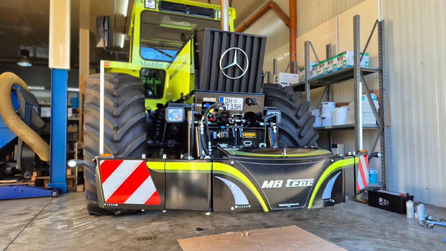 Front weight bumper with reflective red and white panels mounted on a tractor in a workshop with shelving in the background