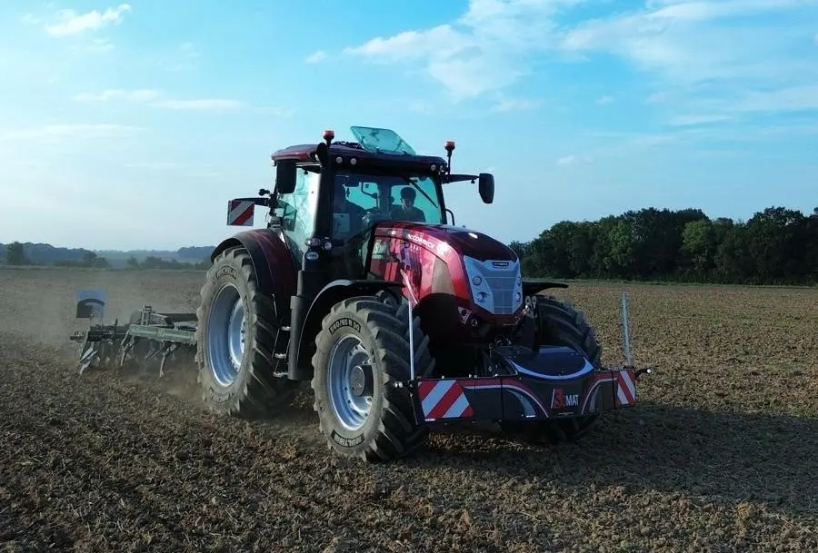Red tractor with a front weight bumper featuring LED lights and safety markings working in a plowed field
