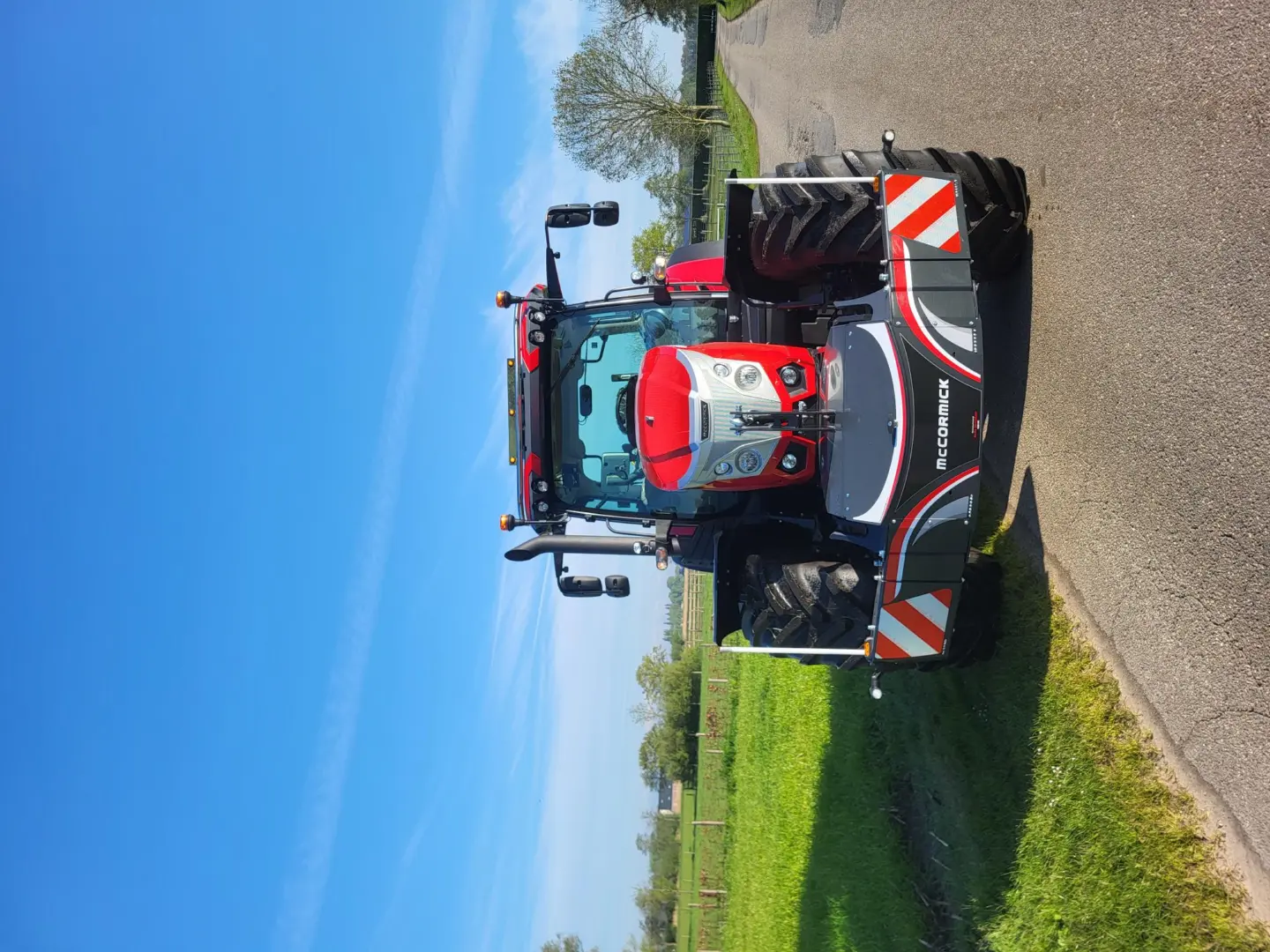 Red tractor with a McCormick front weight bumper featuring LED lights and safety markings parked on a rural road