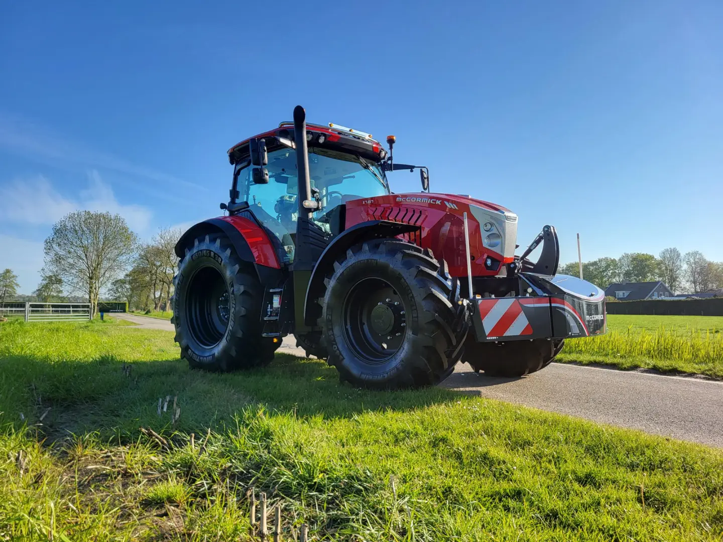 Red tractor with large tires fitted with a front weight bumper featuring LED lights and red-white safety stripes