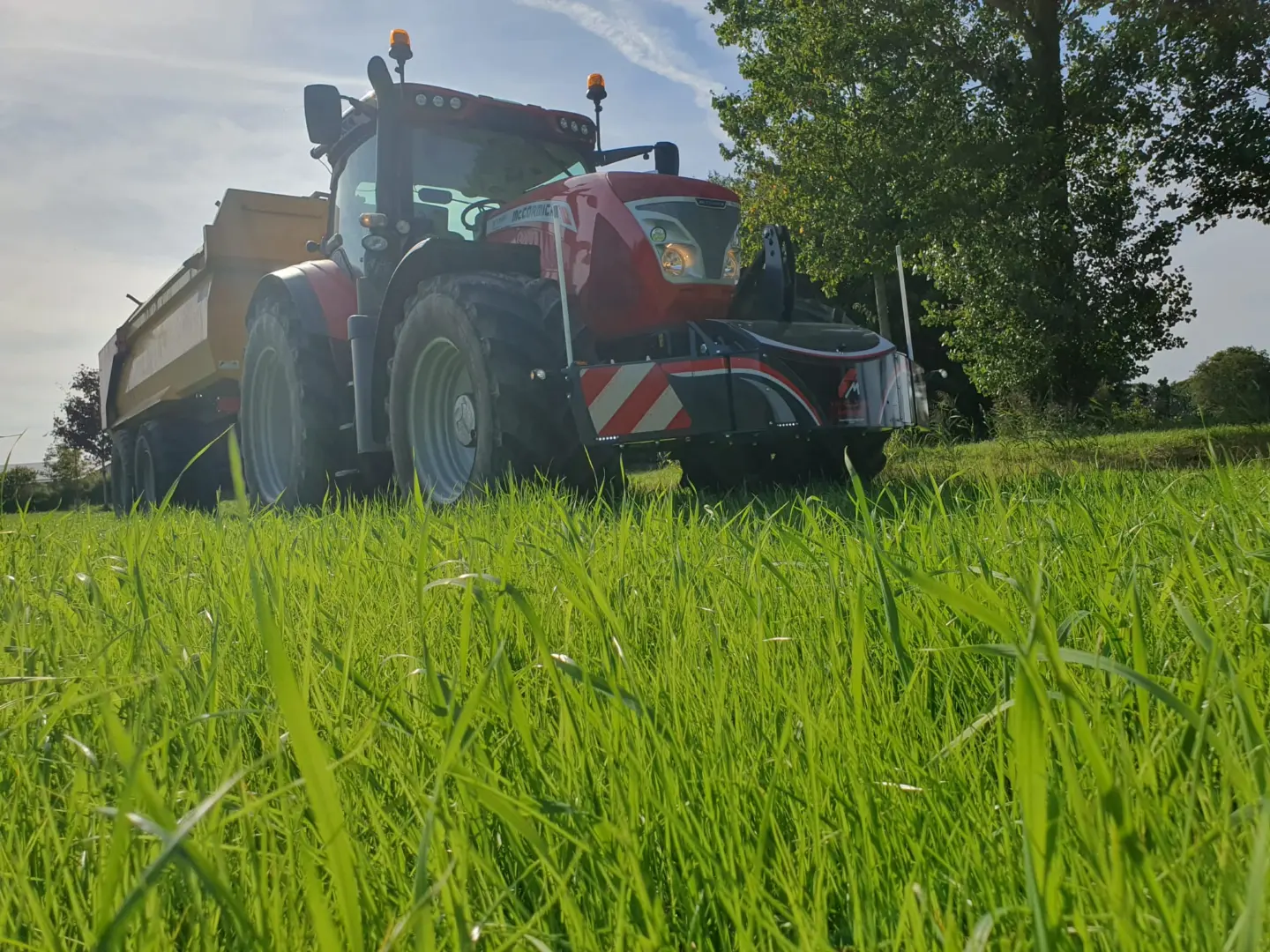Red tractor with a front weight bumper featuring LED lights and safety markings, parked on green grass