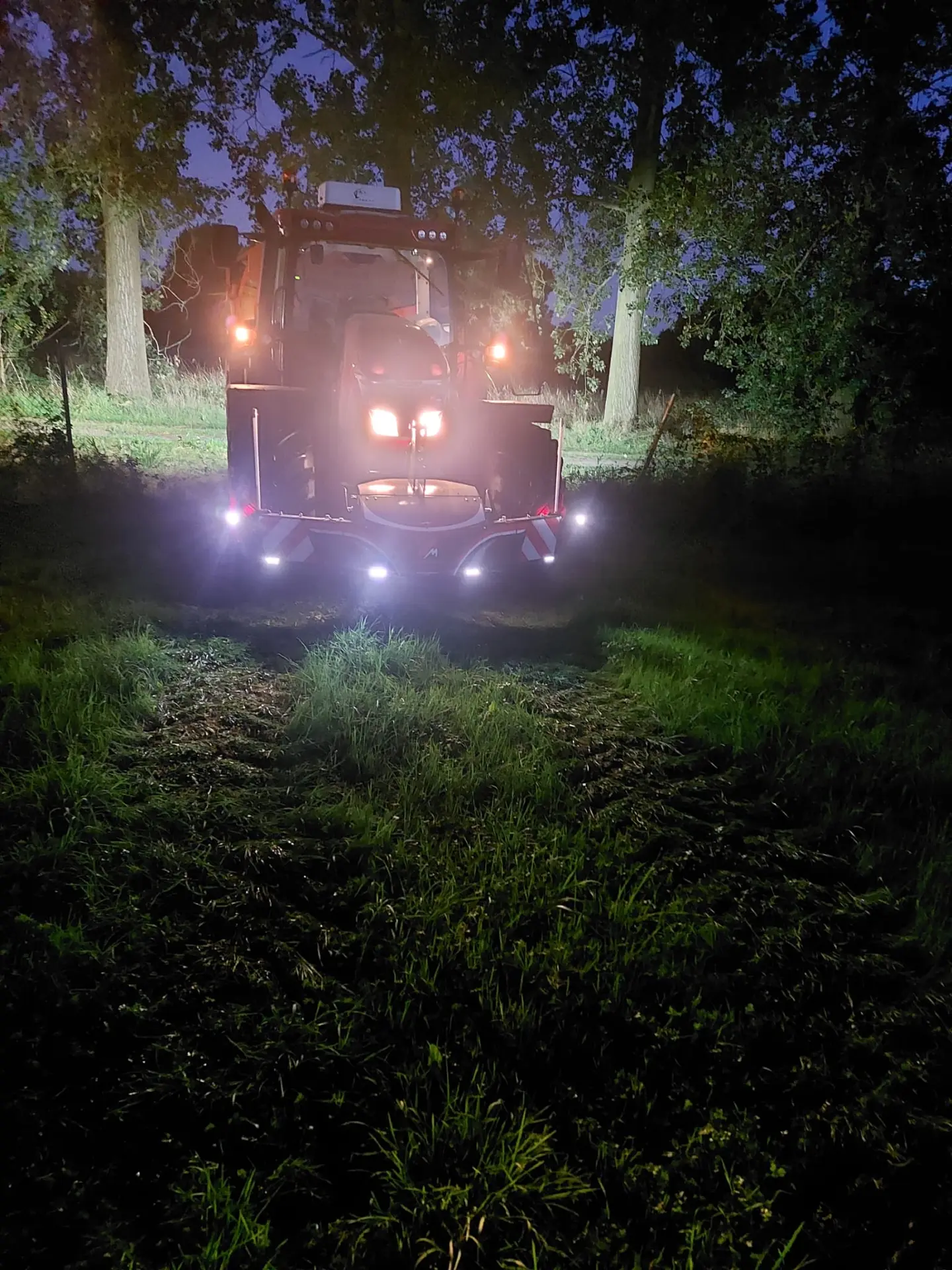 A tractor at night on grass with a front weight bumper featuring multiple bright LED lights illuminated