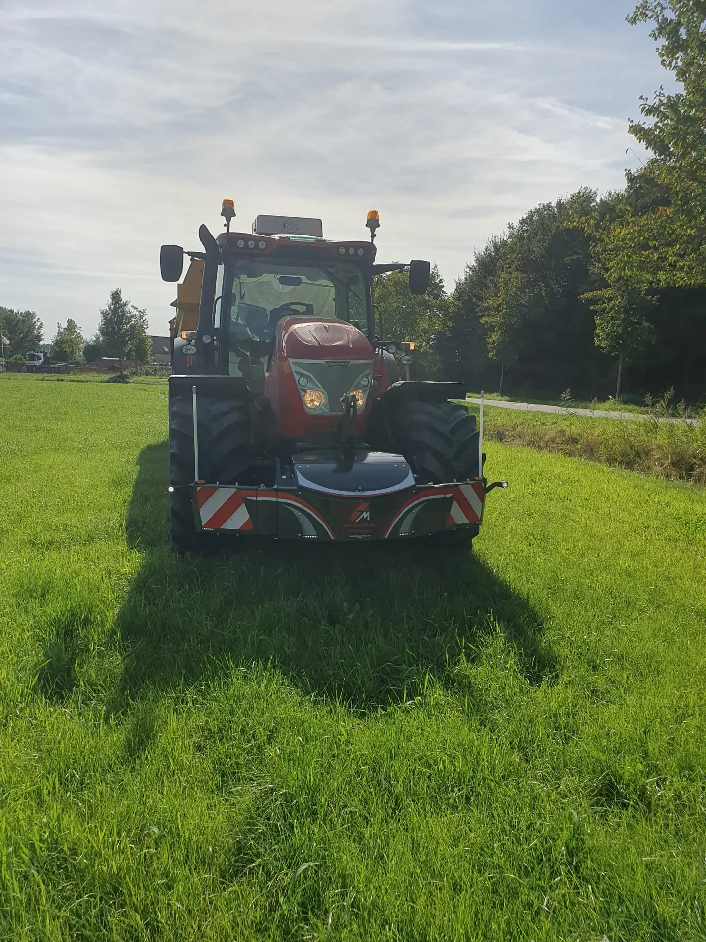 A red tractor fitted with a front weight bumper and LED lights is parked on green grass facing forward