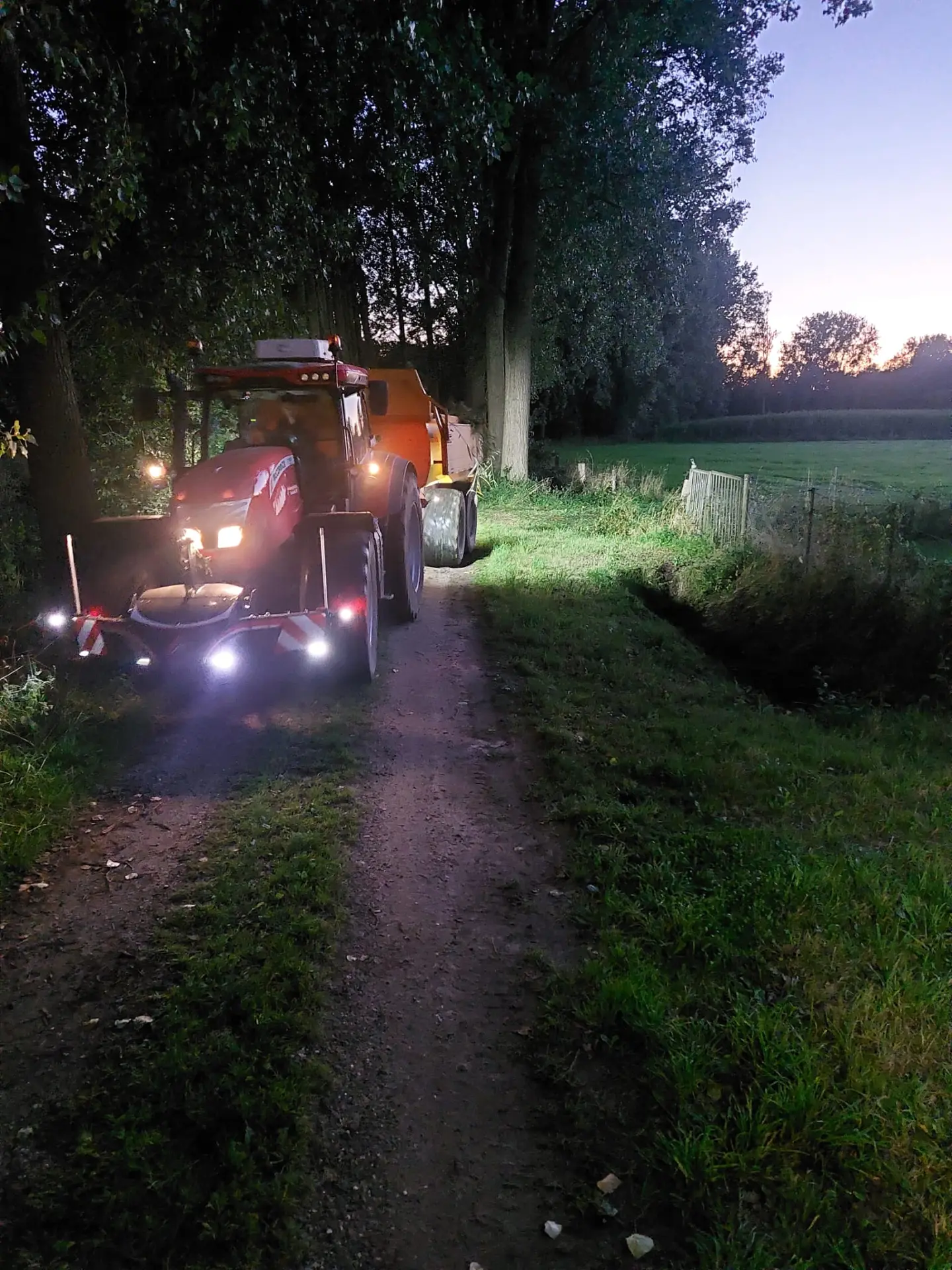 Red tractor with a front weight bumper featuring LED lights is parked on a rural dirt path at dusk