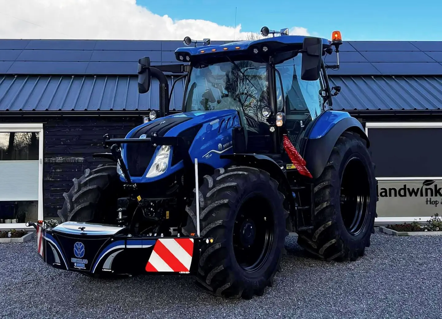 Blue tractor with a large front weight bumper featuring reflective red and white stripes and logo detailing