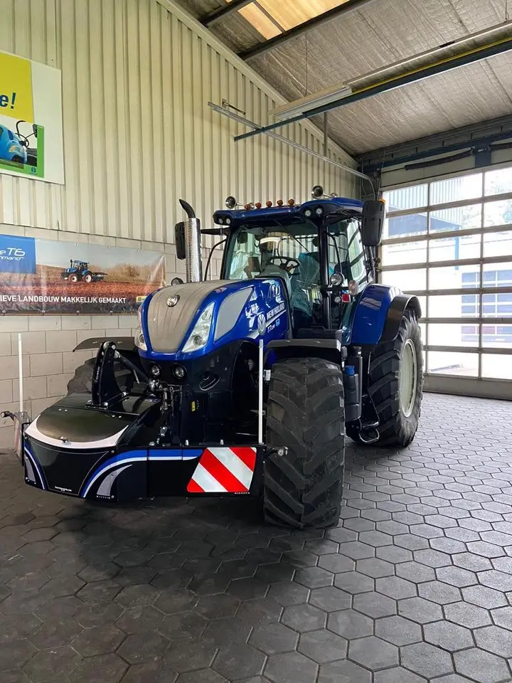 Blue tractor indoors with a black front weight bumper featuring reflective red and white safety stripes