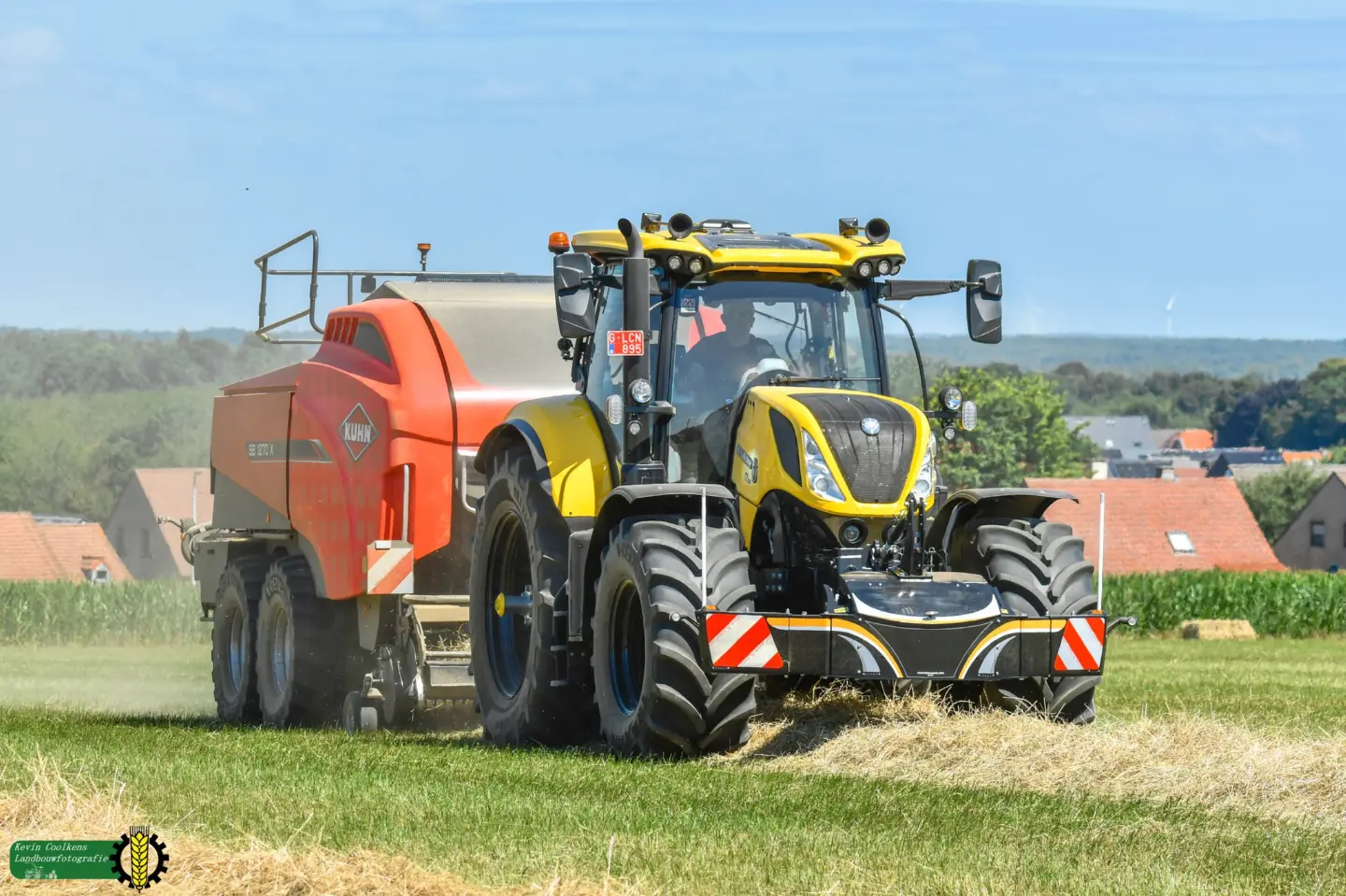 A yellow and black tractor with a front weight bumper and striped markings pulls a large red baler in a grassy field