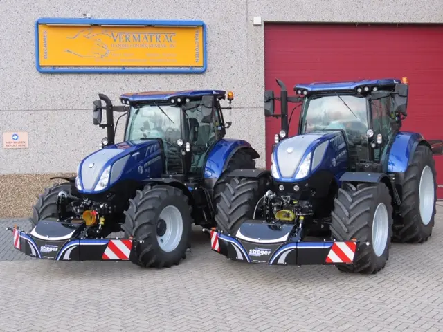 Two blue tractors parked side by side, each fitted with a large black front weight bumper with reflective stripes