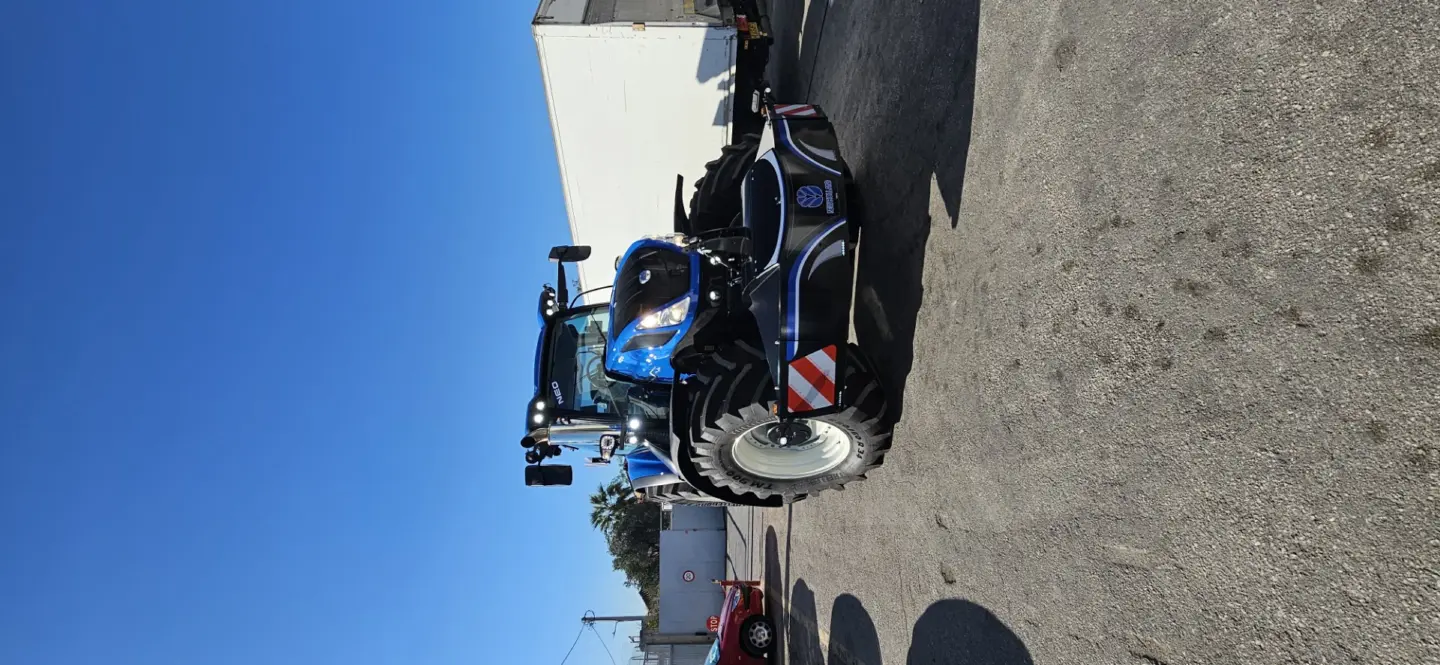 Blue tractor fitted with a large black front weight bumper featuring reflective strips and a New Holland logo