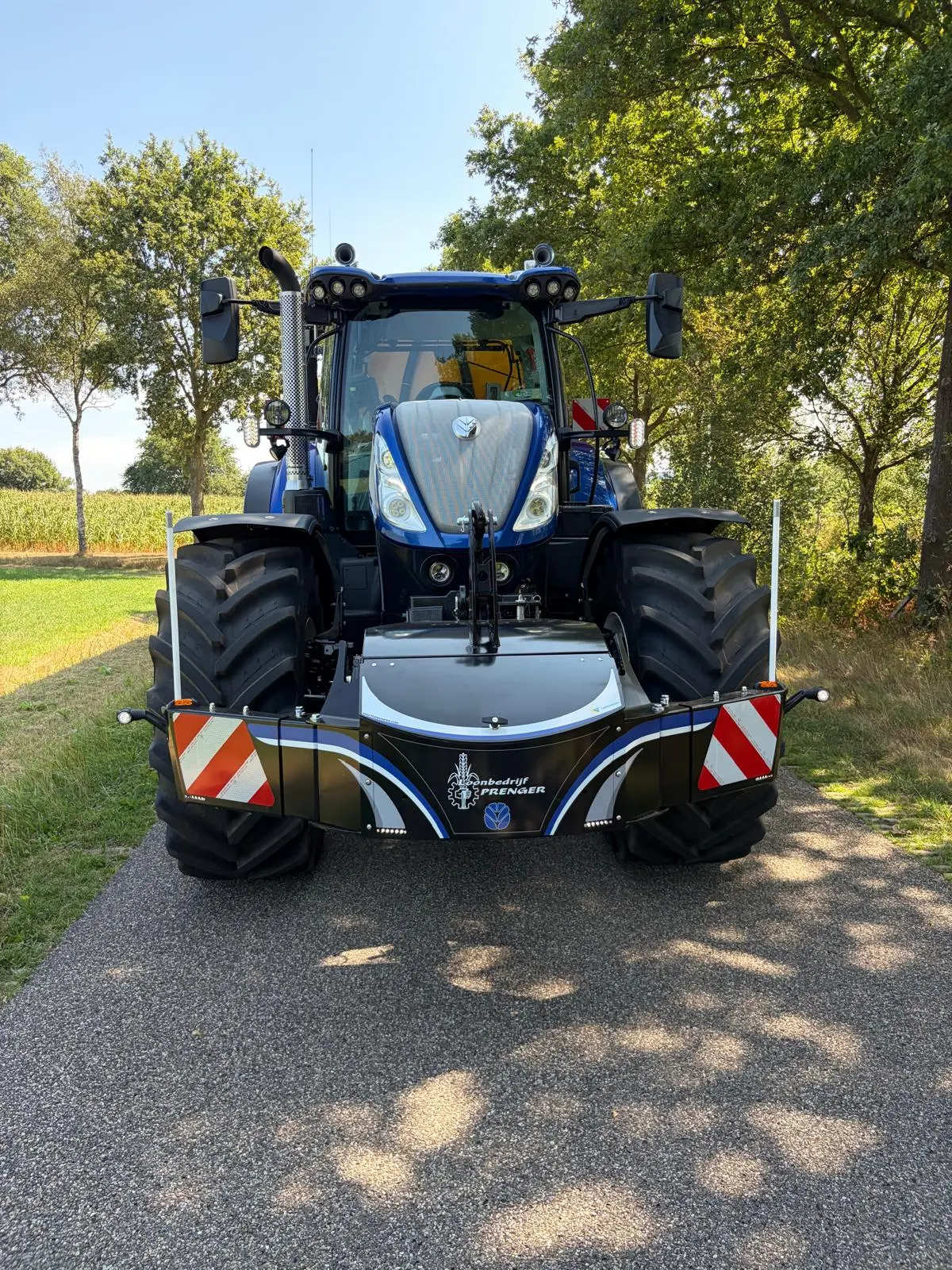 A blue tractor on a rural road with a large black front weight bumper featuring reflective red and white stripes