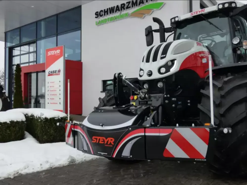 Large red and white STEYR tractor with a front weight bumper installed, parked outside a snow-covered dealership.