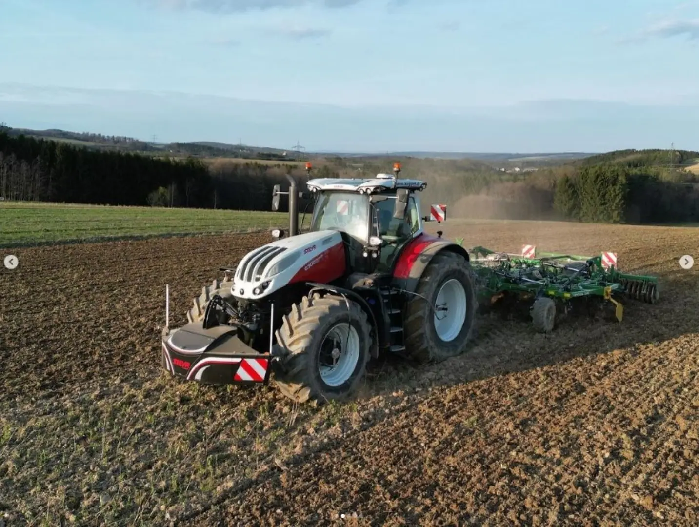 A tractor with a front weight bumper is working on a plowed field with an attached implement.