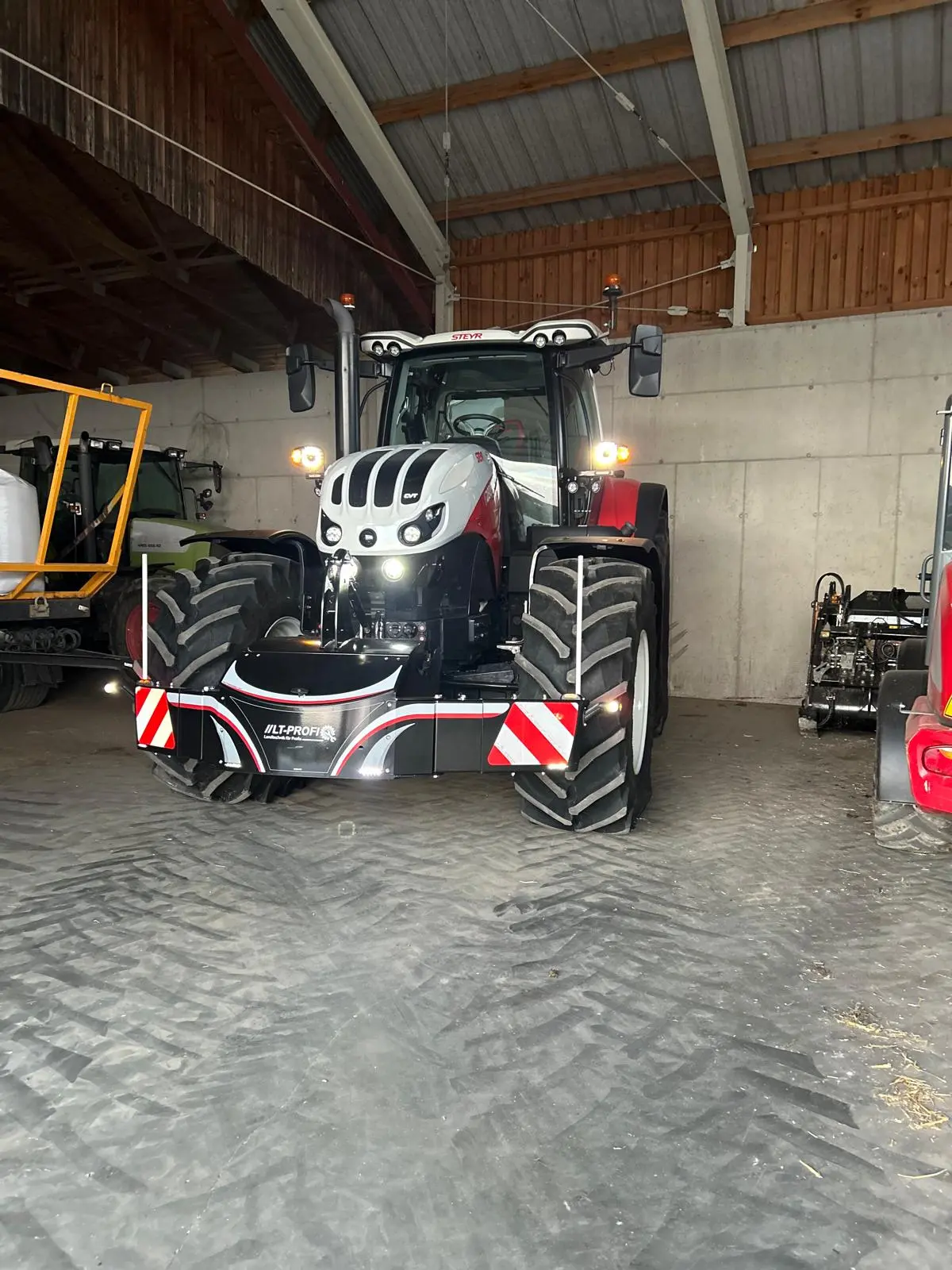 A large tractor fitted with a front weight bumper featuring red and white safety stripes parked in a shed