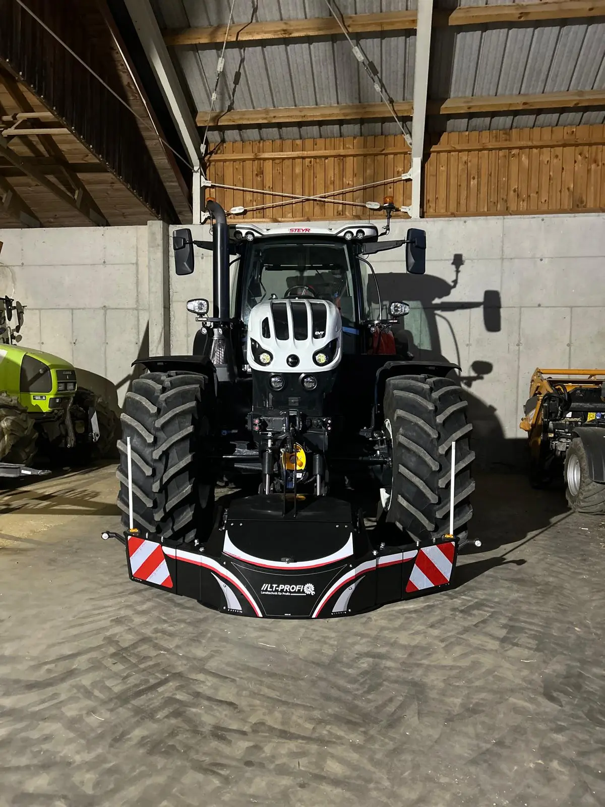 A tractor with a large black front weight bumper featuring reflective red and white stripes in a barn.