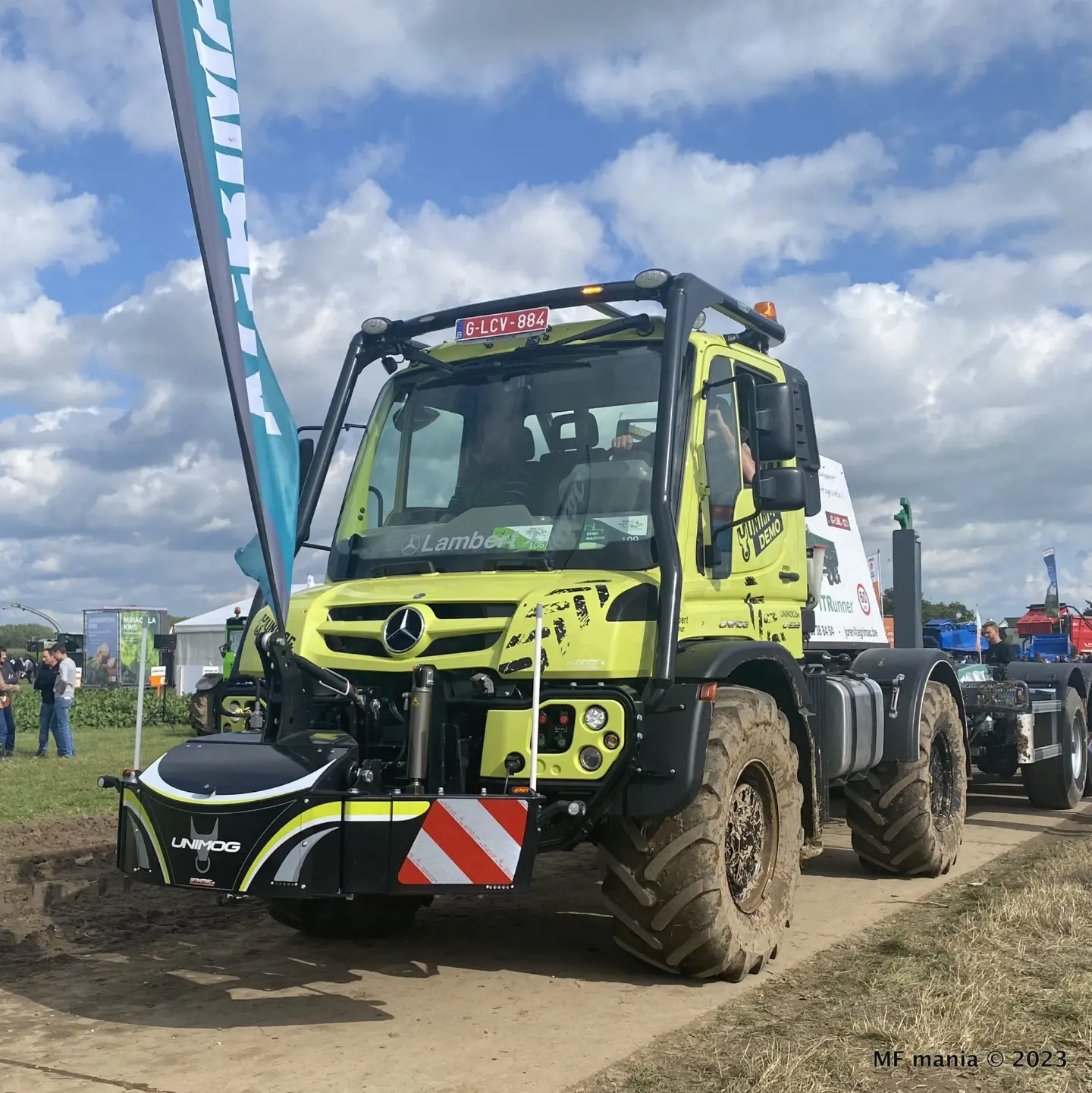 A green Unimog with a black front weight bumper featuring reflective red and white markings on a dirt track