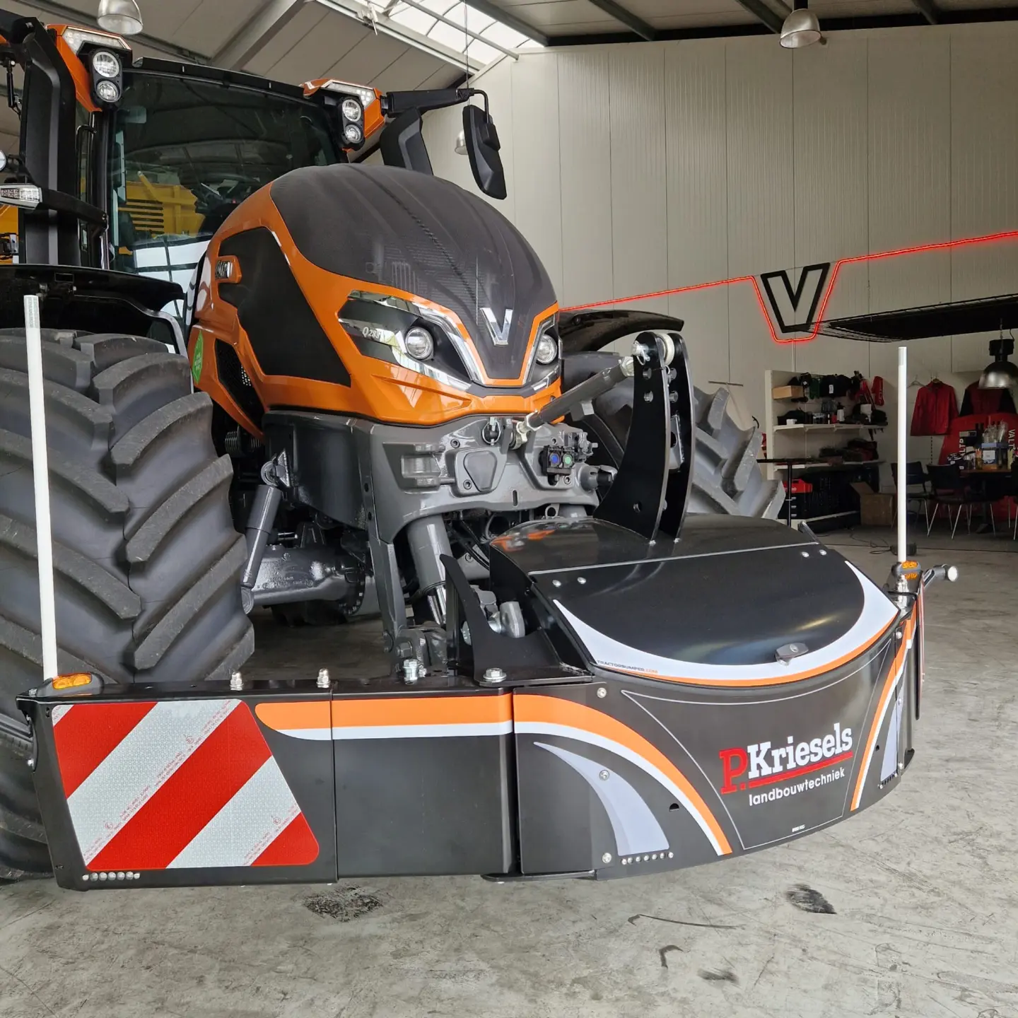 Orange tractor indoors with a large front weight bumper featuring reflective stripes and "P. Kriesels landbouwtechniek" text