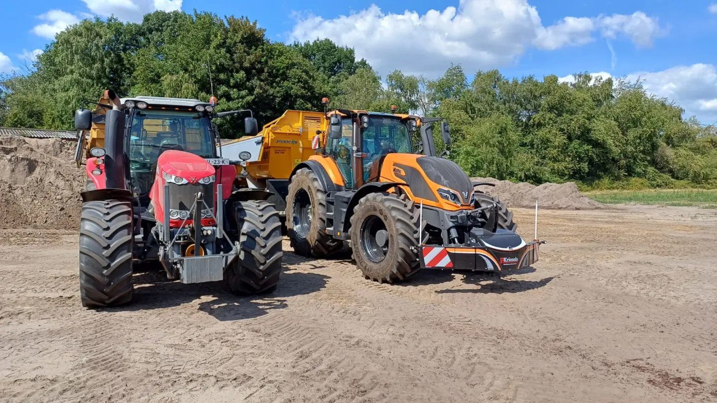 Two tractors with large tires are parked on dirt, one fitted with a black front weight bumper with red stripes.