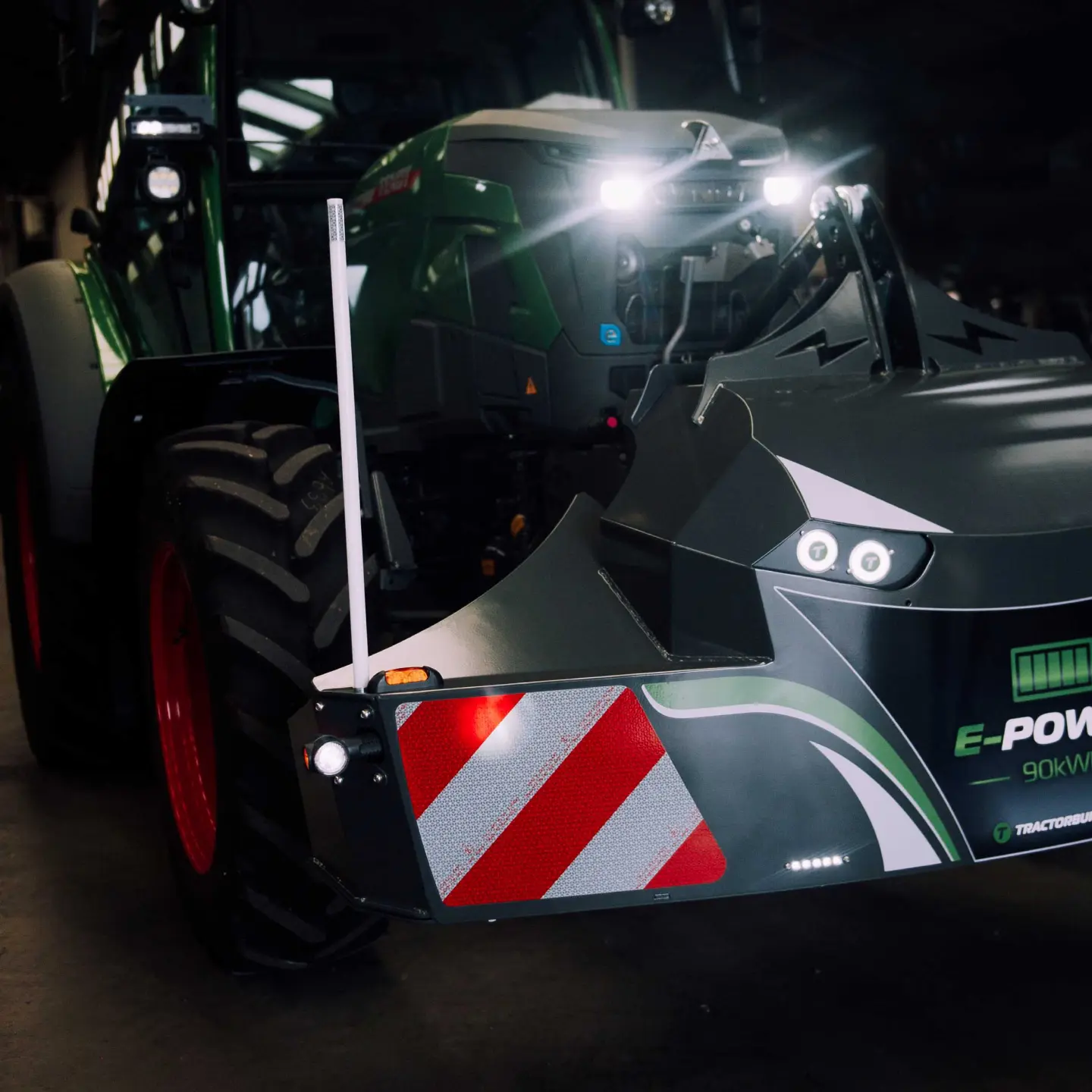 A close-up of a front weight bumper with lights and reflective red stripes mounted on a green tractor indoors