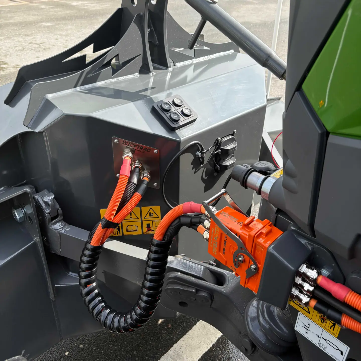 Close-up of a grey front weight bumper with attached cables and connectors mounted on a green tractor.