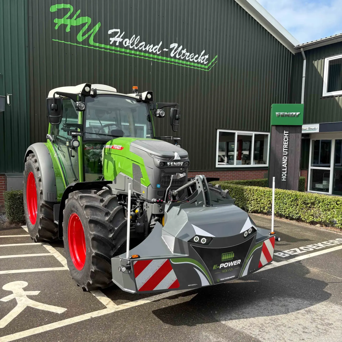 A green tractor with a front weight bumper featuring reflectors, lights and E-POWER 60 kWh marking, parked outside a building