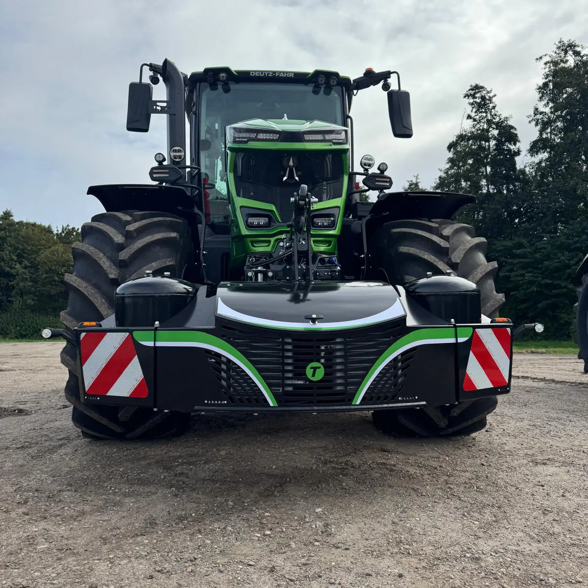 A tractor fitted with a front weight bumper featuring reflective red and white stripes and green accents